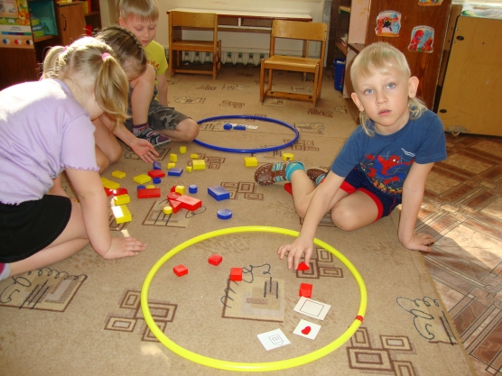Дети играют на полу с блоками Дьенеша и обручами